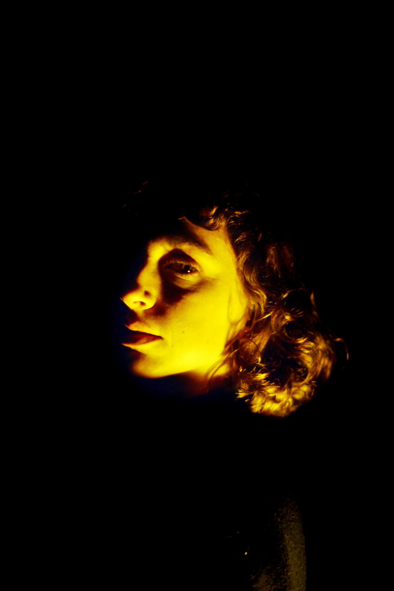 Model looking at the camera, dark background, yellow light on their face