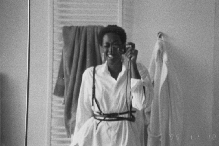 Black and white photo of ria in her bathroom, taking a picture in the reflection of the mirror.