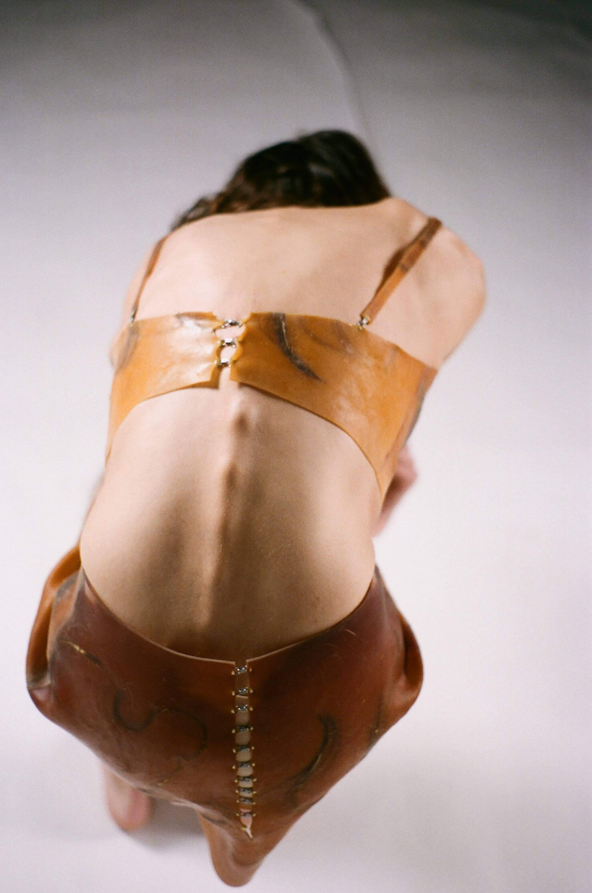 Top shot of the model bent over, their back facing the camera, their spine is the main focus of the shot