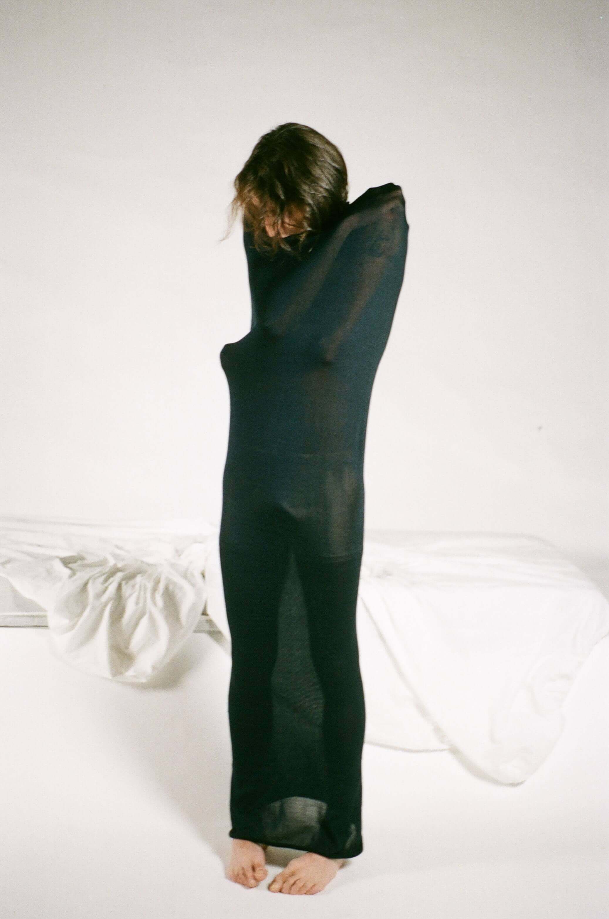 Model wrapped in semi transparent black cloth, standing and hugging themselves